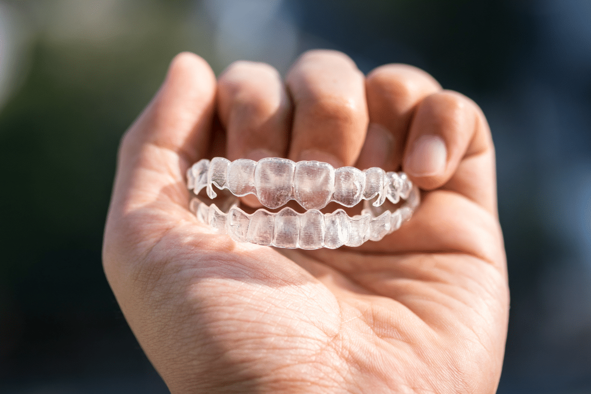 Hand holding clear orthodontic aligner against blurred outdoor background.