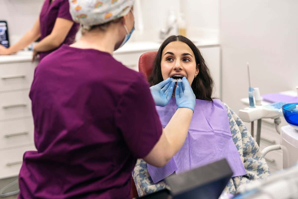 An orthodontic professional fits a clear retainer for a patient, illustrating how retainers help maintain teeth alignment after braces treatment is complete.