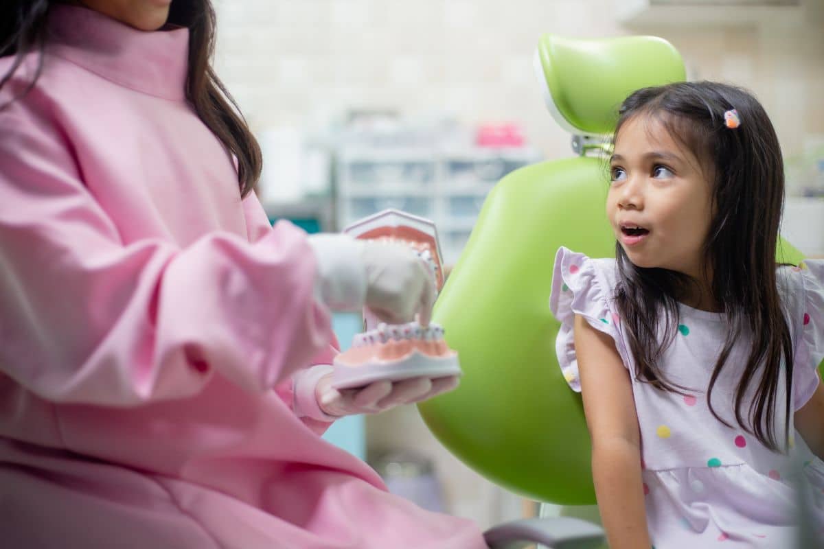 Young child at a dental clinic learning about braces with a dental model, helping parents understand the orthodontic treatment process.