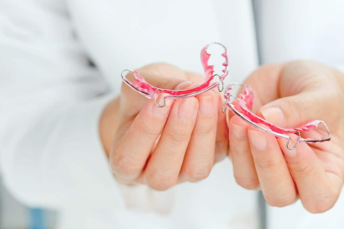 A close-up of removable clear retainers being held by a dental professional, showcasing a common orthodontic appliance used to preserve straight teeth after treatment.